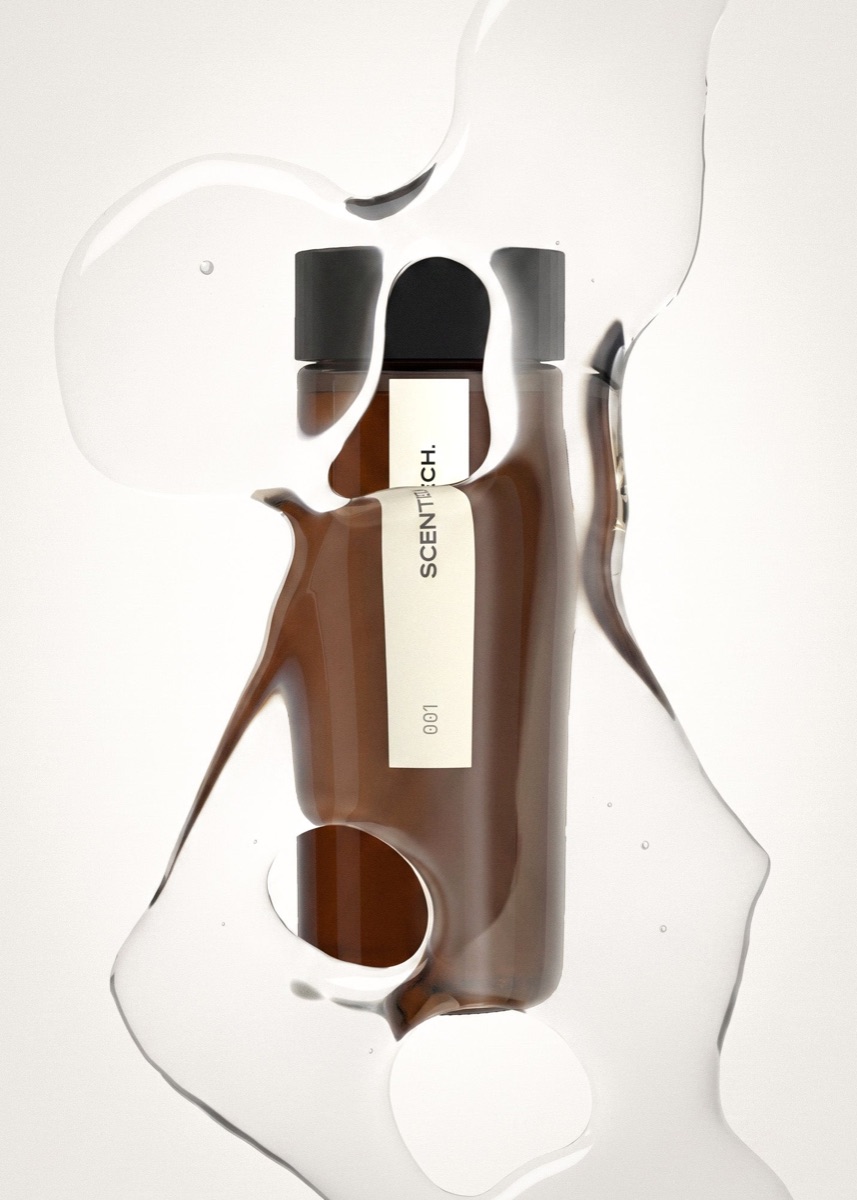 An amber Scentech ScentPod bottle lying on a pale surface, seen through a pool of clear oil that breaks up its outline
